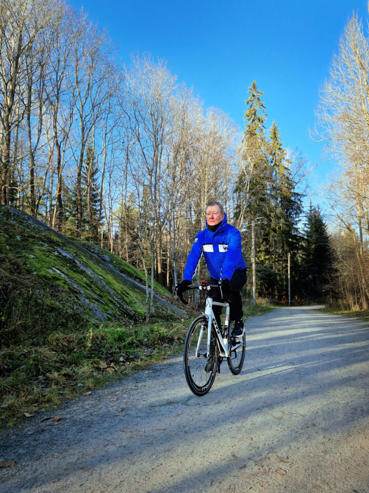 Mies pyöräilee sinisessä takissa aurinkoisena syyspäivänä.