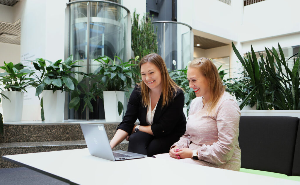 Kaksi naista istuu pöydän ääressä ja katsoo pöydällä olevaa kannettavaa tietokonetta