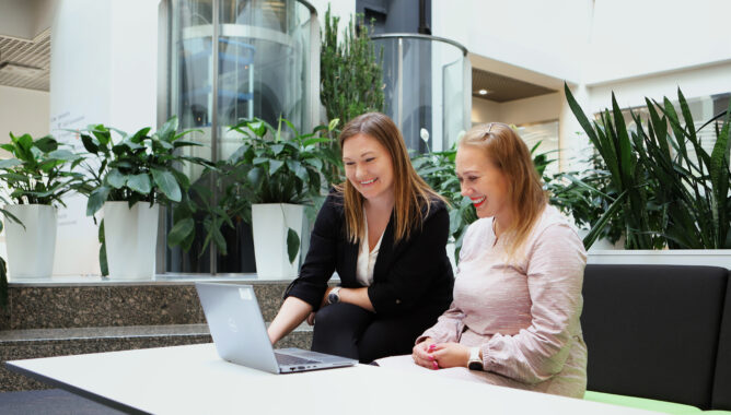 Kaksi naista istuu pöydän ääressä ja katsoo pöydällä olevaa kannettavaa tietokonetta